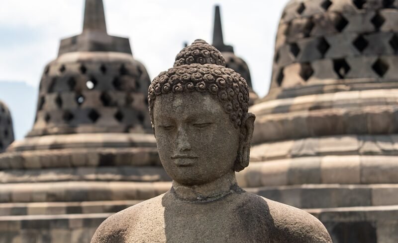 A statue of a buddha sitting in front of a row of stone buildings