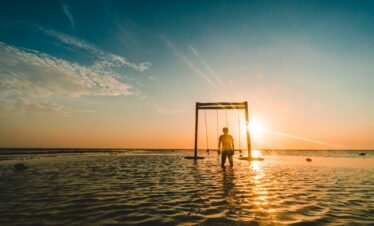 person standing near swing on body of water